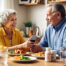 Senior couple enjoying a nutritious meal together, with medication bottles nearby looking at a phone